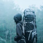 Man Wearing Black Hoodie Carries Black and Gray Backpacker Near Trees during Foggy Weather